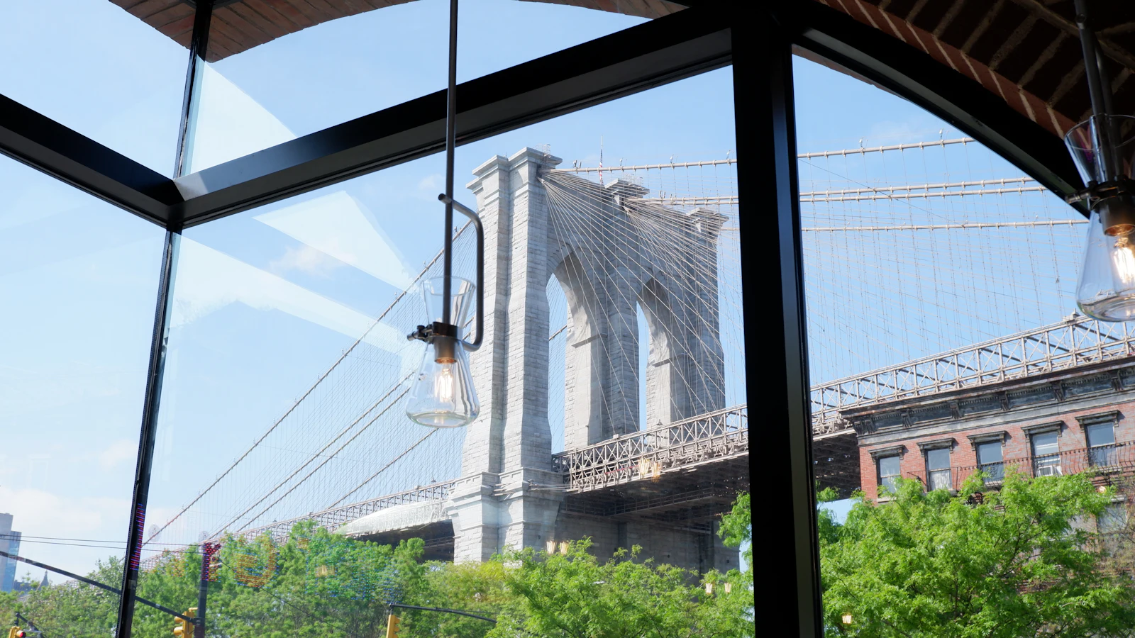 The Brooklyn Bridge seen through a tall window, green trees below