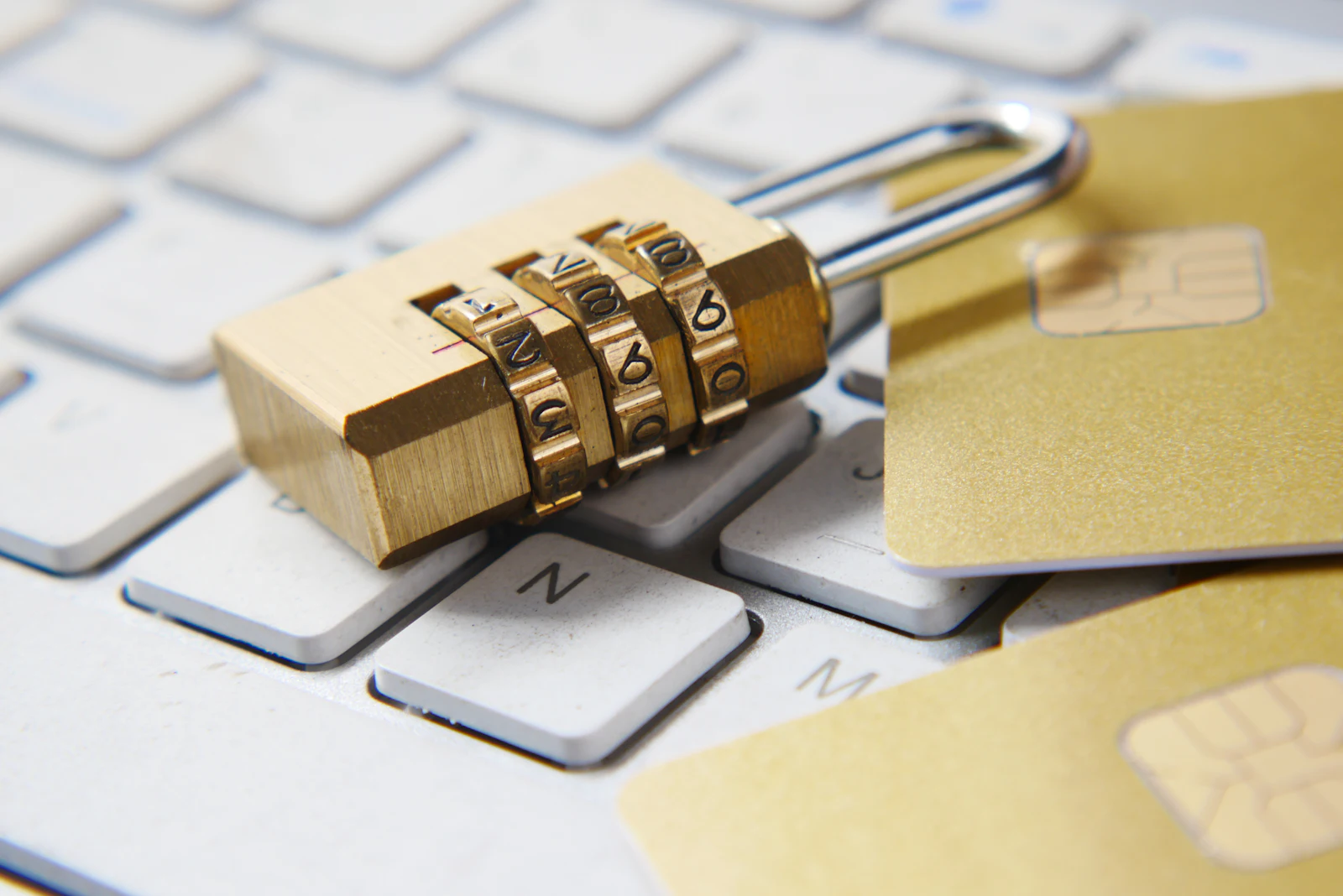 A gold combination padlock resting on a laptop keyboard beside two cards